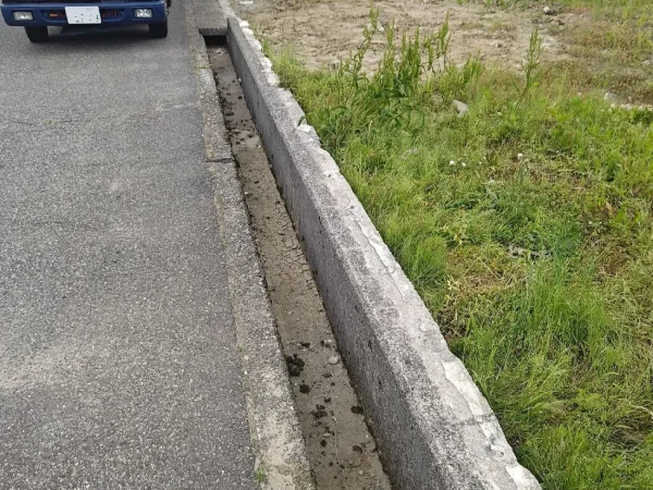 富山の現場写真。道路の側溝の斫り前のコンクリートと株式会社エイキのトラックの写真。側溝の右側が空地、左側が道路です。