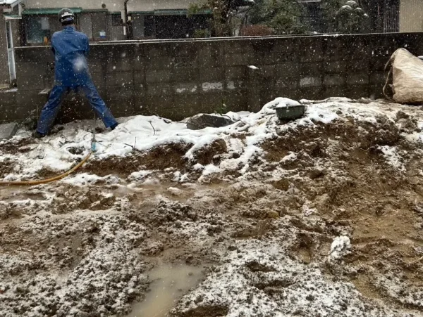 富山市の木造2階建て解体工事現場。株式会社エイキの作業員が雪の中、ブロック塀を解体している写真。