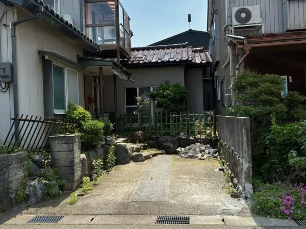 富山の車庫と住宅解体現場。車庫を解体した後の写真。奥に庭石や植栽が見えます。また、隣地との境界までの距離が狭いです。