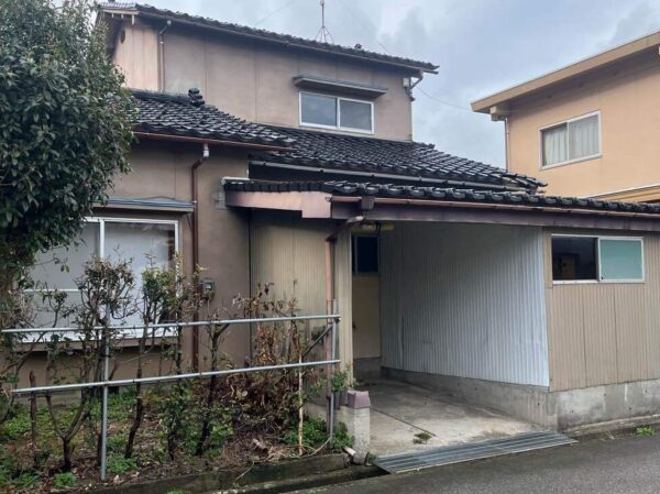 富山市北部の解体前の木造２階建ての住宅。前庭があり、植栽が植わっている。右隣に別の家が建っている