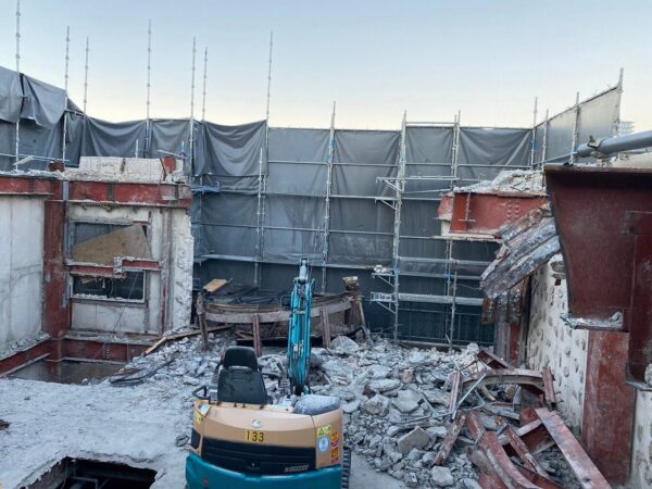 富山市のS造解体現場。養生シートの内側で、構造を確認しながら作業を続ける小型重機 