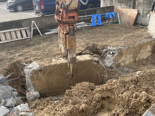  地中の大きなコンクリート基礎を重機で掘り起こし、砕いている様子