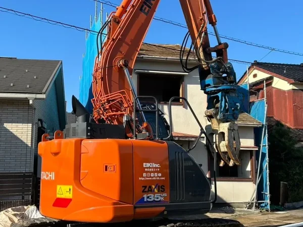 富山市内の住宅街の木造解体現場。3つ並んだ家の前に株式会社エイキのオレンジ色の重機が鎮座している。