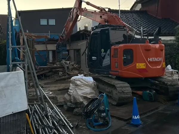 富山市内の住宅街の木造解体現場。狭い隙間に重機を進入させて解体を進めている状況。重機の後ろには青いカラーコーンが置いてある
