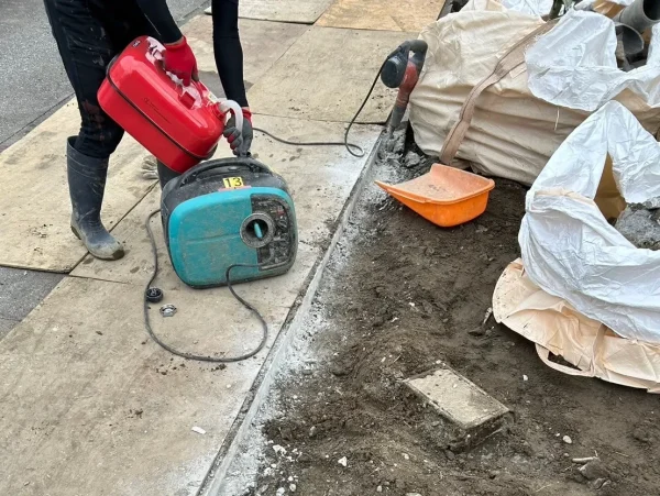 土間部分の斫り作業を進めている様子。電動工具用の発電機に給油を行う株式会社エイキの作業員