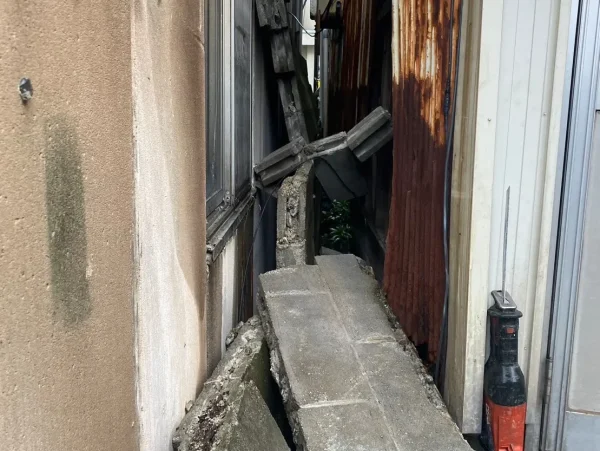 富山市のブロック塀撤去工事現場。狭い隙間からブロック塀のガラを慎重に取り出している様子。工事に使用するレシプロソーも置かれている