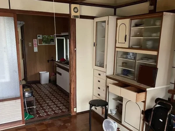 キッチンとリビングの現場写真。食器棚、家電、日用雑貨がそのままの状態です。食器棚には皿も入っています。