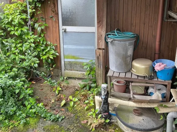 勝手口付近の写真。ホースやバケツ、植木鉢など外回りの備品が写っています。
