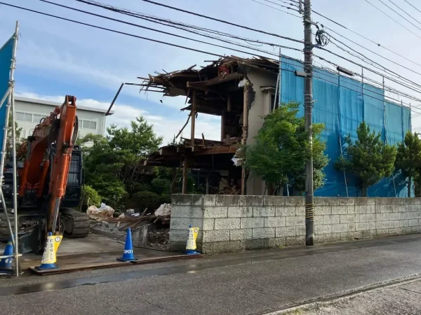 住宅本体を解体する様子。周囲への防塵対策としてブルーシートの養生を行い、散水を徹底してホコリの飛散を防ぎます。