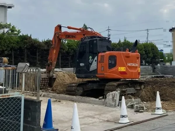 オレンジ色の重機が基礎部分を解体し、盛り上がった地面を整えている様子。