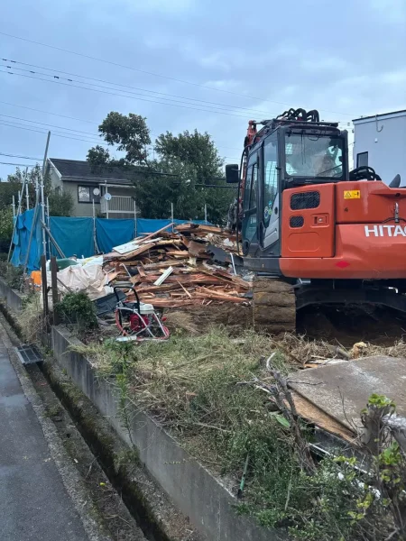解体後の木材建材が積み上げられています。その横には、重機油圧ショベルがあります。
