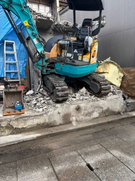 小型重機が屋根部分を解体中。お隣の壁を傷つけないよう、数センチ単位の繊細なレバー操作が求められています。