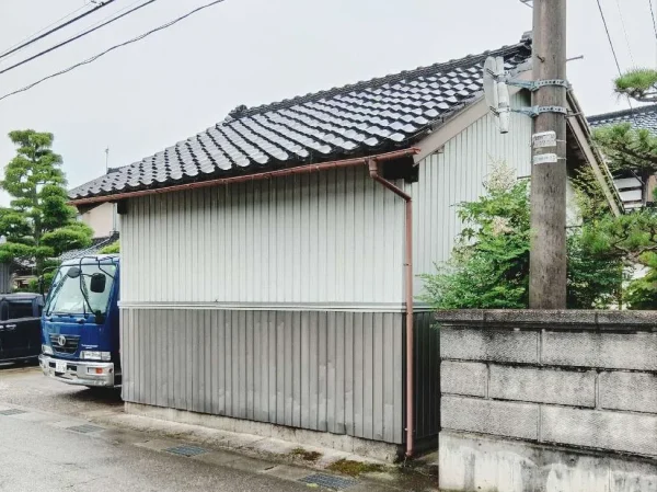 今回の現場である富山市の西部に建つ納屋の写真。瓦と壁がリppにみえる。右側が隣家。