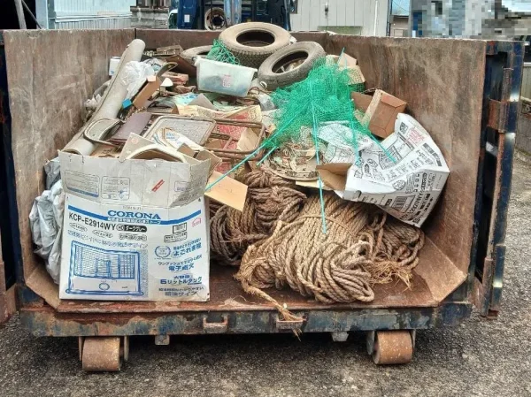 不要物を入れるコンテナ。その中には、縄・段ボール箱・タイヤ・木製品など多種の不用品が積み込まれている。