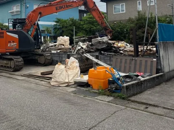 重機、油圧ショベルが見えます。廃材を材質ごとに集め、フレコンバックに詰め込みます。手前にみえる基礎コンクリートは、これから撤去します。