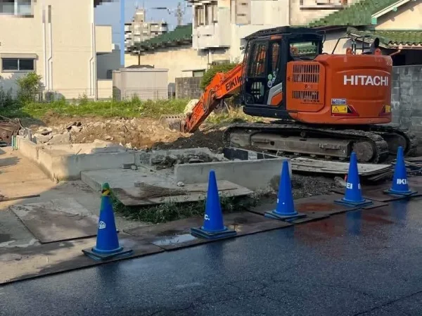 建物本体が解体済みの写真。手前に基礎コンクリートが見えており、株式会社エイキの重機が基礎コンクリートと地中の埋設物を撤去している。