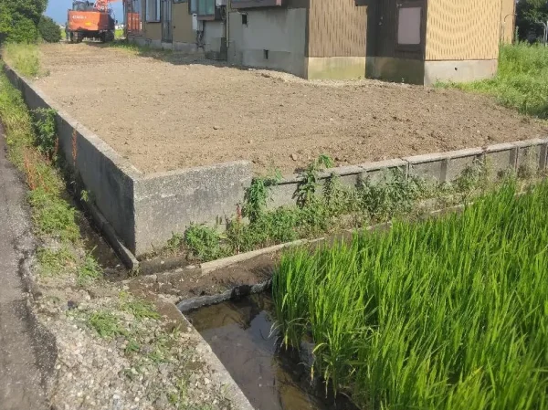 納屋が解体され、更地が出来上がっている。作業を終えたオレンジ色の重機が現場から離れている