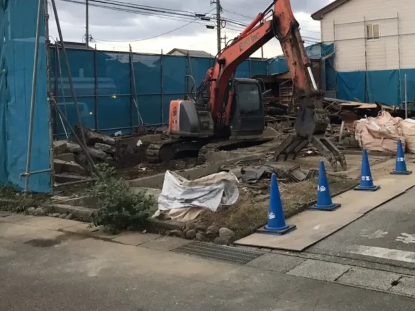 富山市で株式会社エイキのオレンジ色の重機が木造住宅を解体中。現場の周辺は青いシートで養生されている
