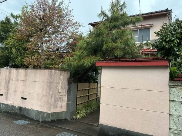 富山市の解体現場。二階建ての木造住宅を植栽と塀が取り巻いている。