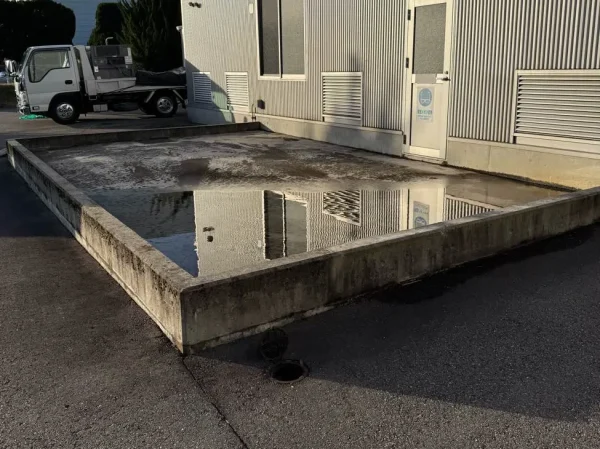 工場の隣に、コンクリートの外構（土間）がある。低い覆いで囲まれている。