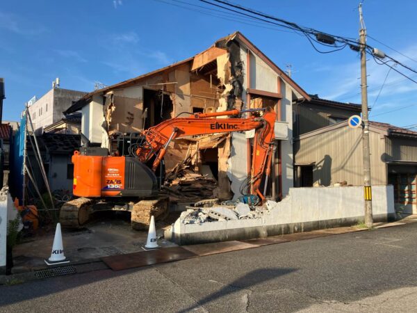 住宅を外部から重機を使って解体中。重機には、弊社エイキの文字が書かれてある。