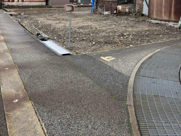 街中の空地。手前は道路。奥の２面は住宅。建物や外構がなく更地となっている。