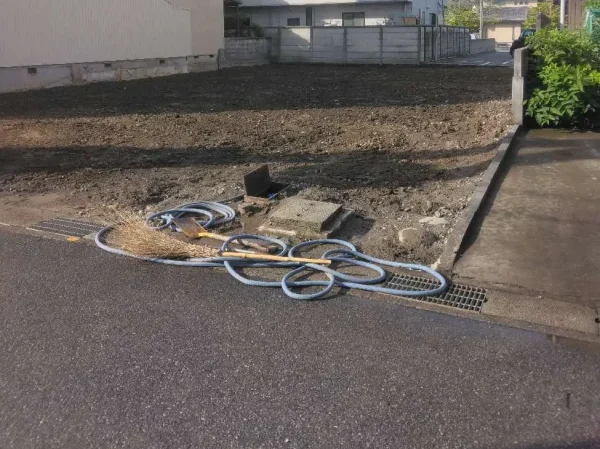 解体撤去が終わり、土地が更地になった状態の写真。清掃と散水に使用した箒とホースが置いてある。後に全て片付けて撤収