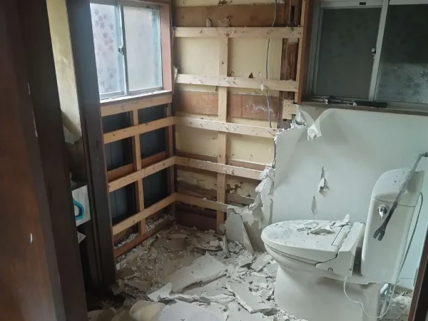 壁が解体され、石膏ボードの破片が散らばったトイレ