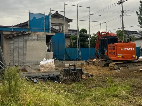 オレンジ色の重機が動き、足場とシートに囲まれた解体途中の現場。母屋はほぼ解体している。