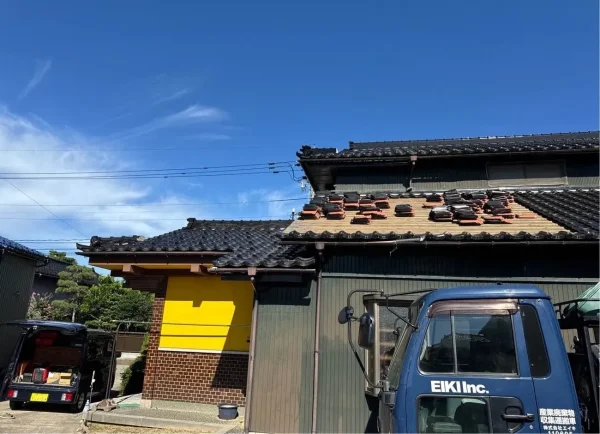 瓦を剥がし屋根の上で整理されている写真。家の前にはエイキのロゴが入った紺色のトラックがある