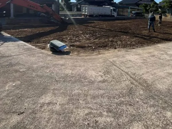建物とコンクリート基礎を解体し終え、更地を作っている。左側にはエイキの重機、右側には従業員が二人配置されている。