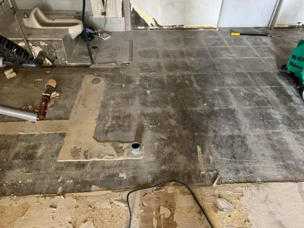 床材が剥がされ、コンクリートの跡が見えている写真 左上に、剥き出しの便器が見える。