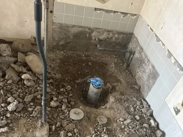 タイルの床が壊され、配管が露出している写真。壁のタイルはまだ残っている。