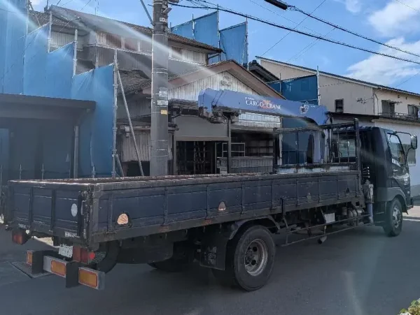 写真の中央にトラック帆の写真。後ろには住宅。この住宅を解体した時の廃材をトラックに積み運搬する。
