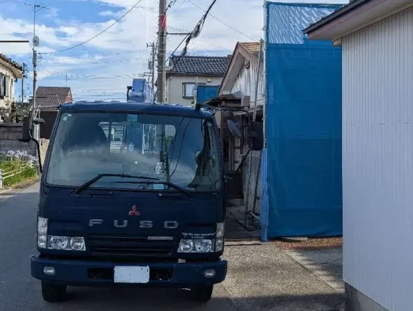 トラックの前方写真。右側が住宅。養生の青色シートが見える。