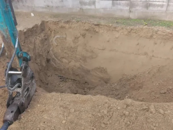 土を掘った写真。左側に青色のユンボ。アタッチメントをつけている。