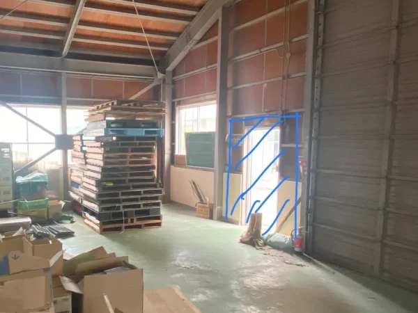 倉庫の内部の写真。倉庫内にはパレットや資材が積まれています。青いマーキングが拡張予定の範囲です。 