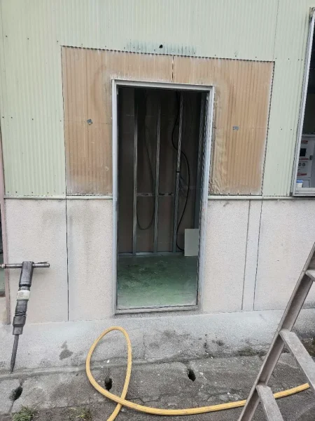 倉庫の出入り口の外観写真。サッシを撤去済み。コンクリート箇所を拡張する用具、ブレーカーが左下に置いてある。