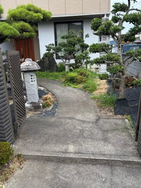 施工前の庭の全景。真ん中にコンクリートででできた通路、その左右に灯籠と植栽が見える写真