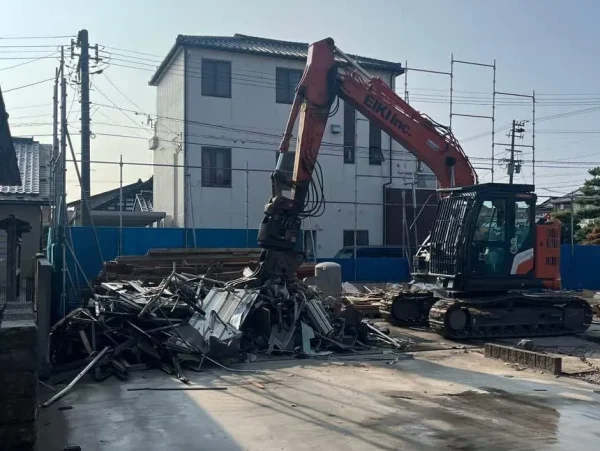 解体した建材を材質ごとに分別している重機の姿。株式会社エイキのロゴが入ったオレンジ色の重機が鉄の廃材を掴んでいる