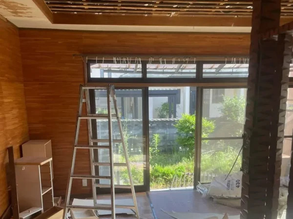 内装解体中の住宅の一部屋の写真。天井がはがれている。床材も剥がされている。脚立が見える。