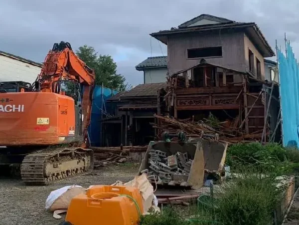 住宅の躯体を重機で解体している写真。住宅の周囲は青色シートで囲ってあります。