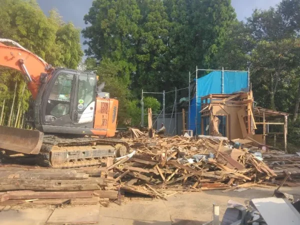 住宅の骨格がほぼ解体終了。手前には解体廃材が写っている。奥にはブルーの養生が写っている。