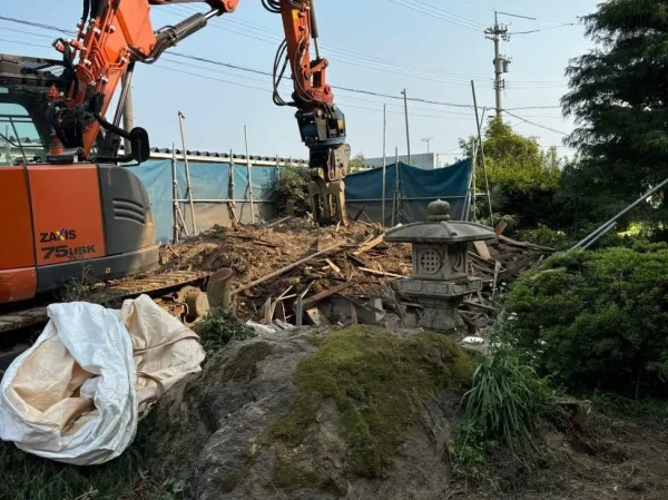 油圧ショベルを使って庭木などを解体撤去中。手前に大きな庭石が見える。