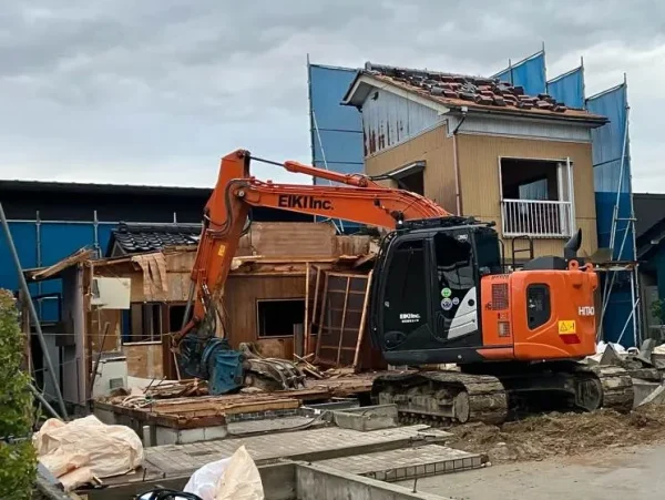 家屋を重機で解体中。周囲は青色シートの養生が見える。