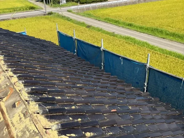 納屋の屋根。瓦を下におろす前の写真。あたり一面に田んぼが広がっている
