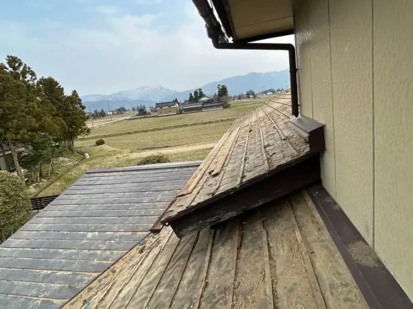 屋根の様子。瓦を撤去し、下地の木材（野地板など）だけにした状態。遠くに山が見える。
