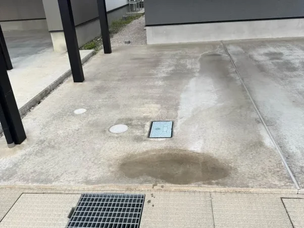 カーポートの下のコンクリート土間。地面には水道や排水の点検口（マス）が設置されている。カーポートの黒色の柱も見える。