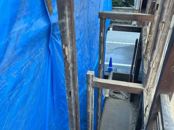 隣家との隙間が写っている。わずかな隙間。左の家の壁は青色シートで養生されている。