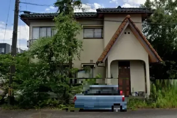 ２階建ての現場住宅。緑に囲まれている。前道には車。